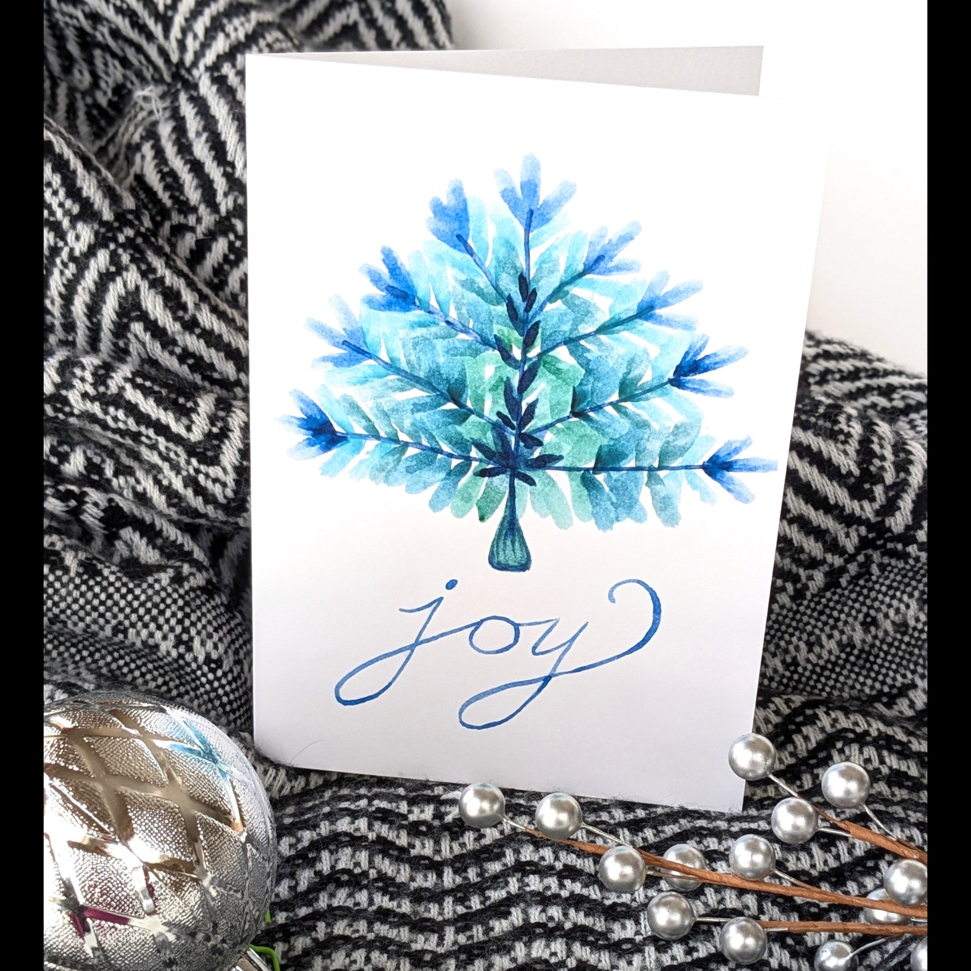 Card with blue tree design and 'Joy' text on a textured surface with decorative elements.